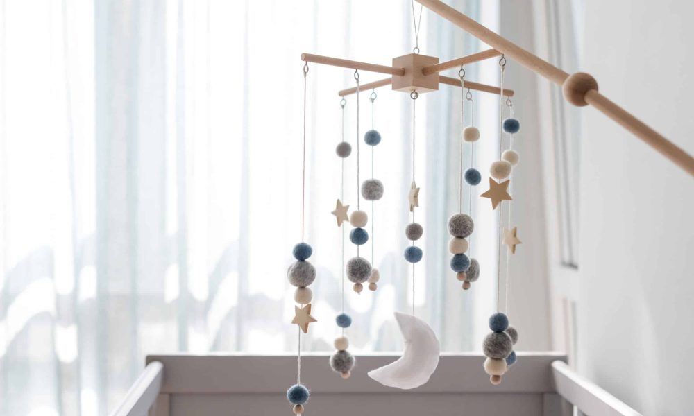 Baby crib mobile with stars, planets and moon. Kids handmade toys above the newborn crib. First baby eco-friendly toys made from felt and wood hanging in light room. Space for text.